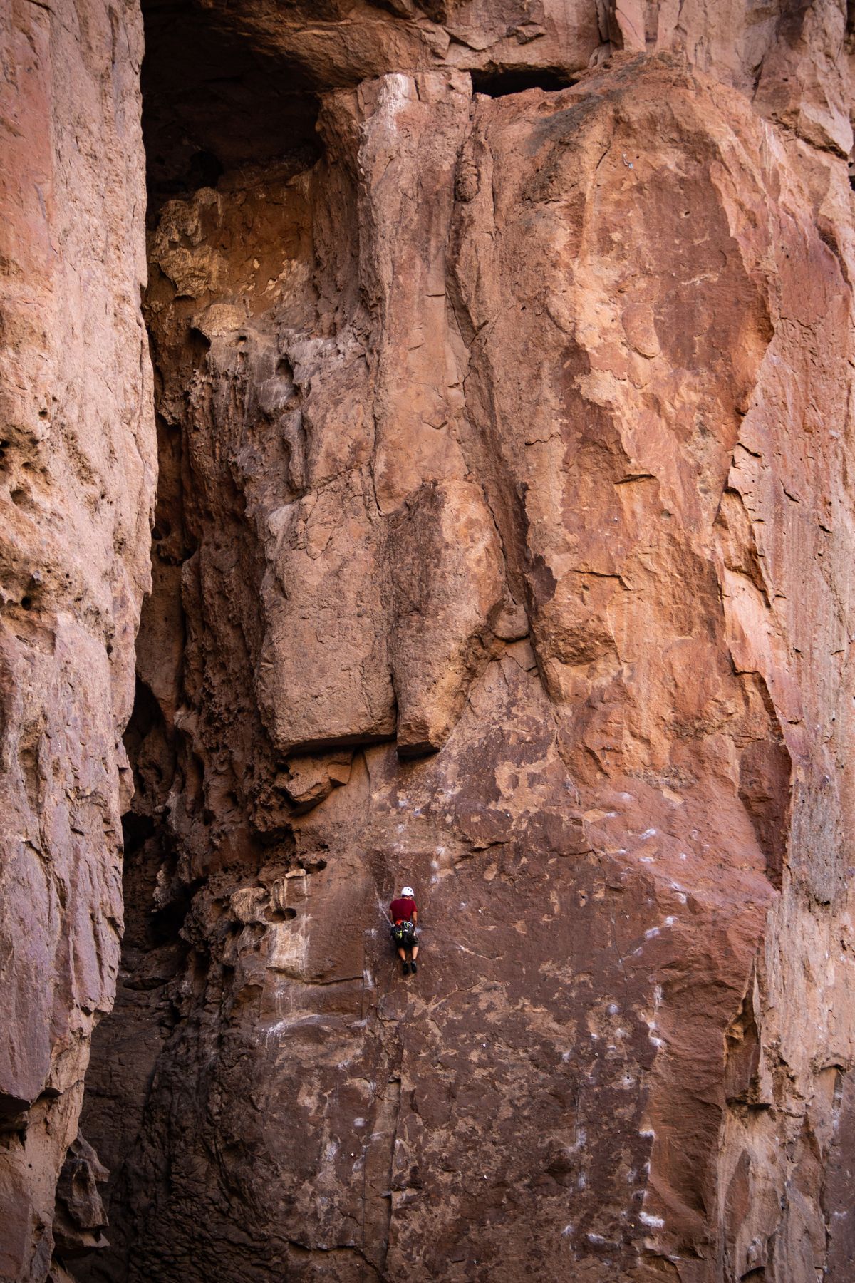 A climber in red ascending a vast rock face
